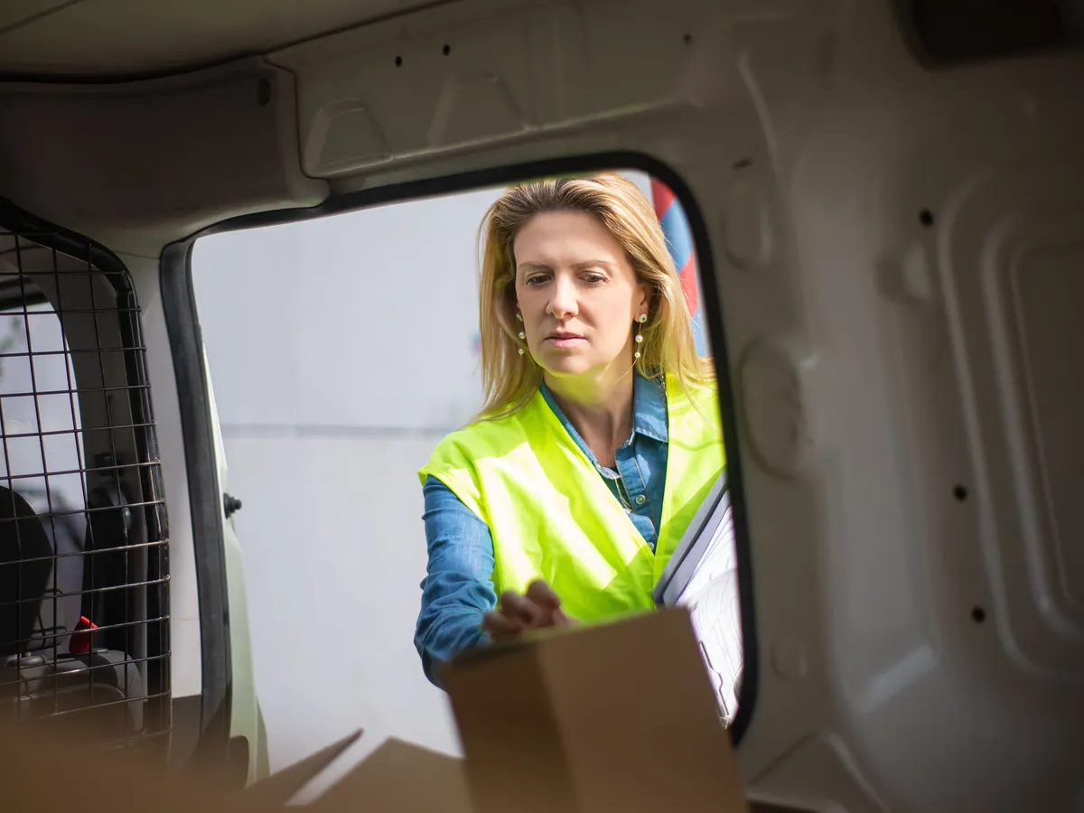 A courier in a hi-vis vest lifting a parcel from the back of a delivery van.